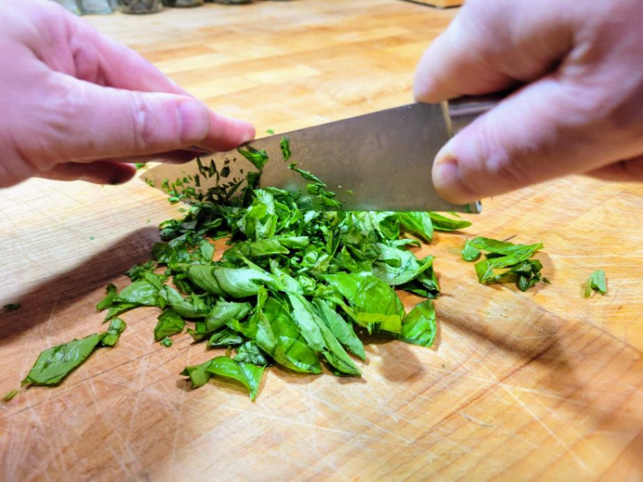 Chopping herbs (basil) on butcher block cutting board