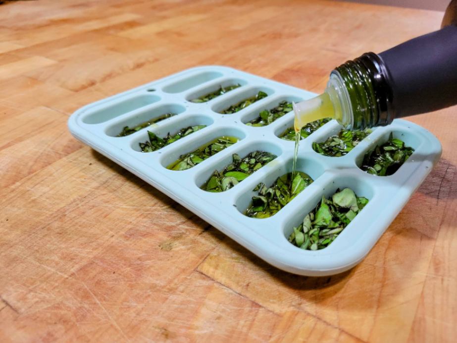 Pouring oil into herb filled ice cube tray for freezing