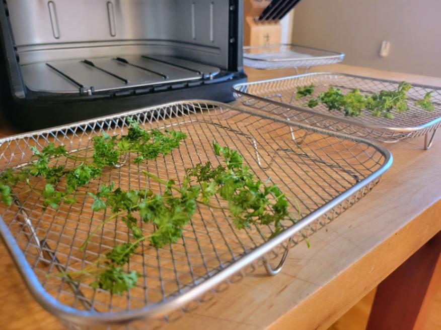 Dried parsley in air fryer baskets on butcher block counter