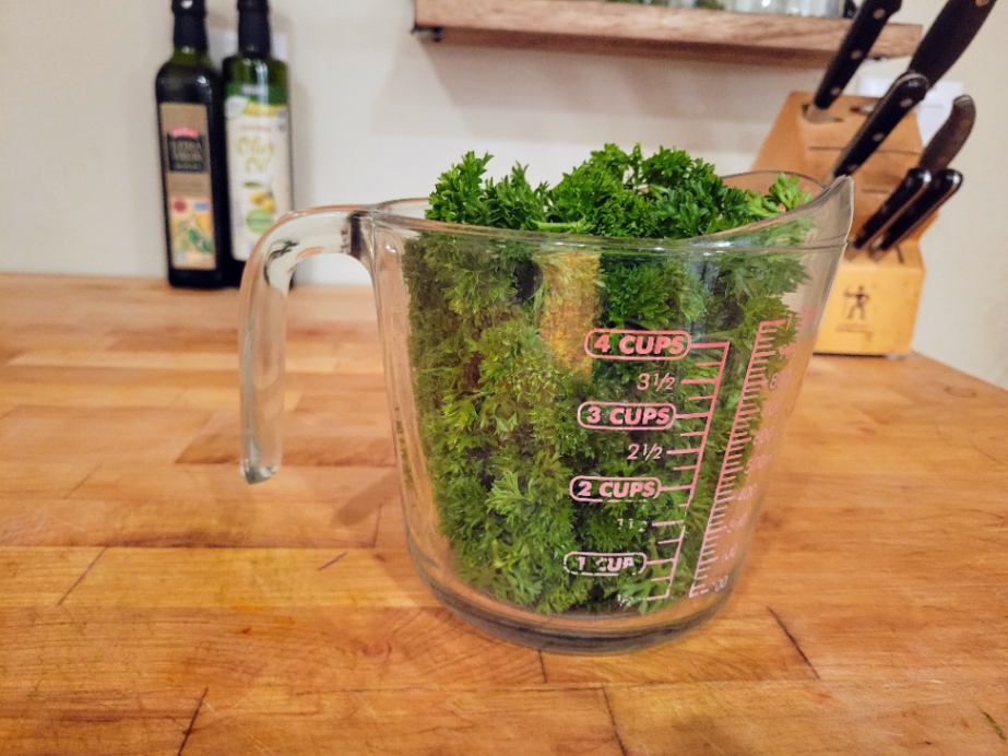 bunch of curly parsley measuring 5 cups in a large measuring cup on a butcher block counter